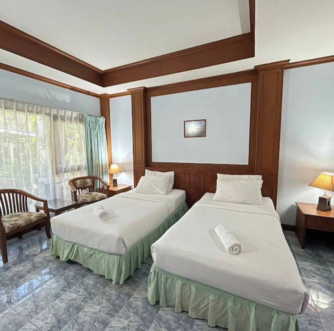 A hotel room with two beds, a chair, a table, and a window with curtains.