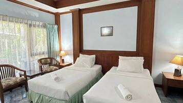 A hotel room with two beds, a chair, a table, and a window with curtains.