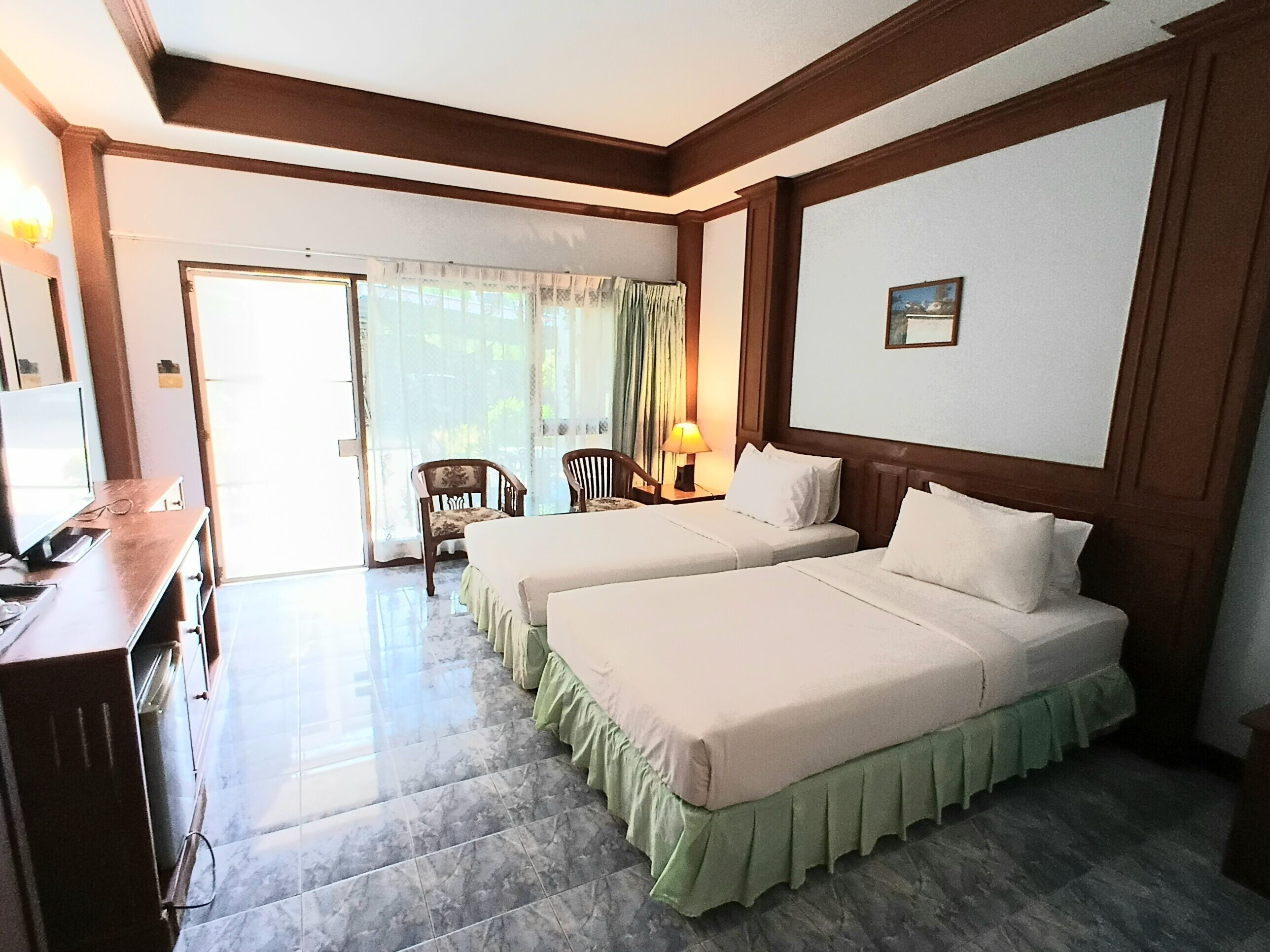 A hotel room with two beds, a desk, a chair, and a view of the outdoors.