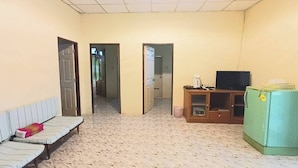 Una habitación con un sofá, un televisor sobre un mueble de madera, un refrigerador y una puerta que da a otra estancia.
