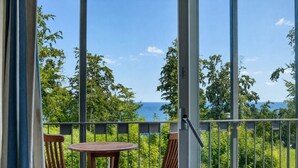 Un balcón con dos sillas de madera y una pequeña mesa redonda, con vistas a un paisaje verde exuberante y al mar.
