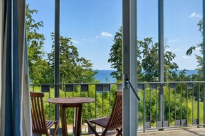 Ein Balkon mit zwei Holzstühlen und einem kleinen runden Tisch, mit Blick auf eine üppige grüne Landschaft und das Meer.