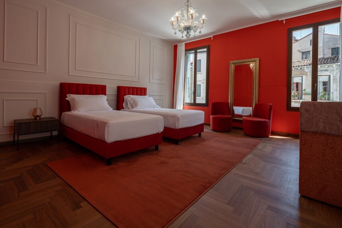 Une chambre d’hôtel avec deux lits, un mur d’accent rouge, un lustre et une vue sur l’extérieur.