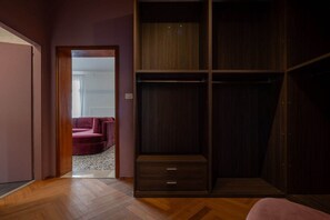 Una habitació amb un terra de fusta, un armari amb diversos calaixos i un sofà vermell al fons.