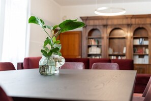 Una taula de dinar amb un vas de vidre transparent que conté una planta, situada en una habitació amb cadires tapissades de color vermell i una prestatgeria de fusta al fons.