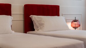 Quarto de hotel com duas camas, cada uma com cabeceira vermelha e roupa de cama branca.