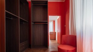 Um corredor com um guarda-roupa, uma cadeira vermelha e uma porta para outro quarto.