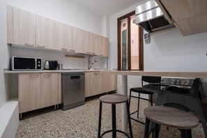 A compact kitchen with a microwave, coffee maker, dishwasher, and a gas stove. There are two stools and a small table. - Venetian Velvet (Venice)
