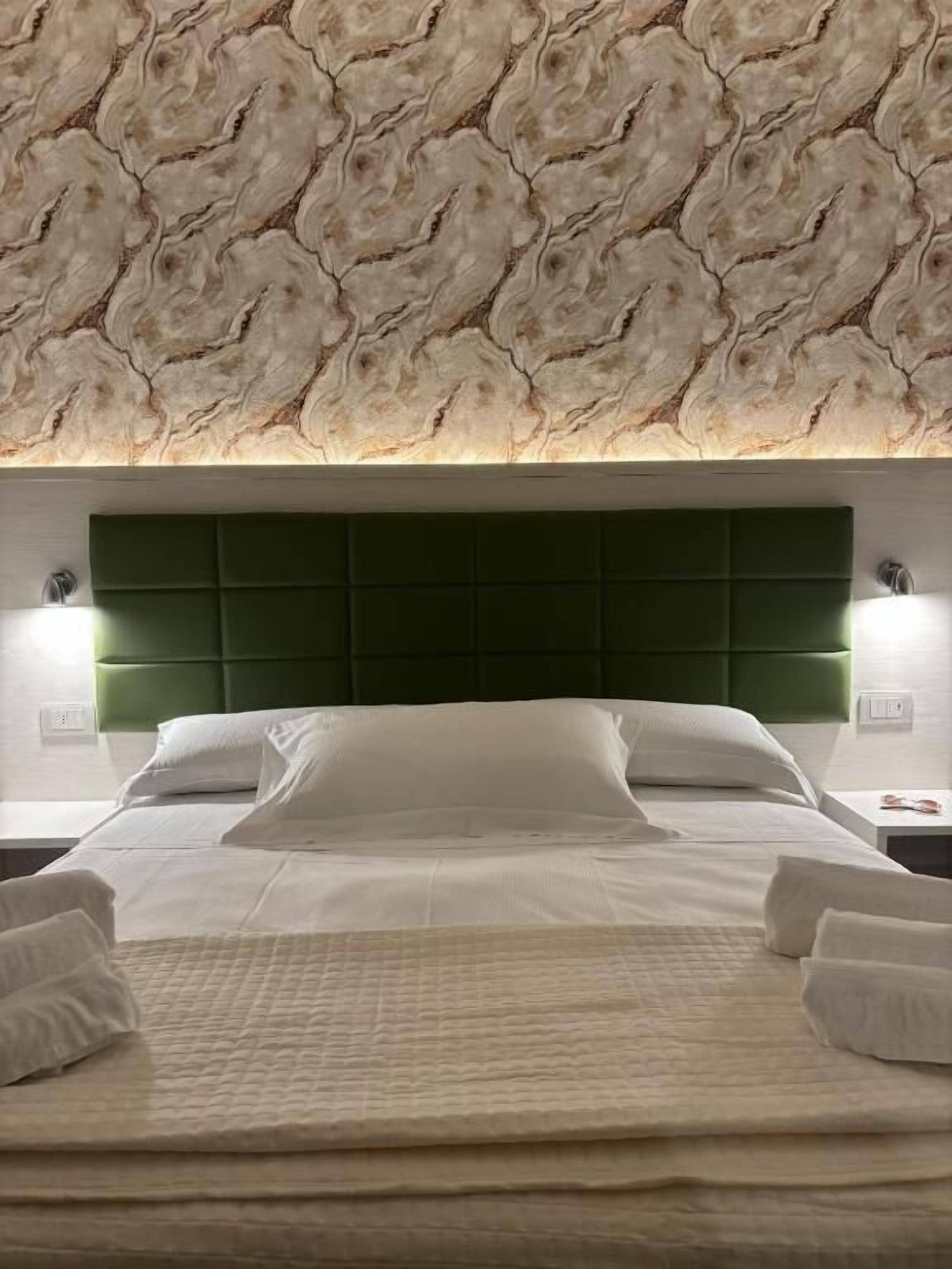 Une chambre d’hôtel avec une tête de lit verte, du linge de lit blanc et un plafond à motifs.