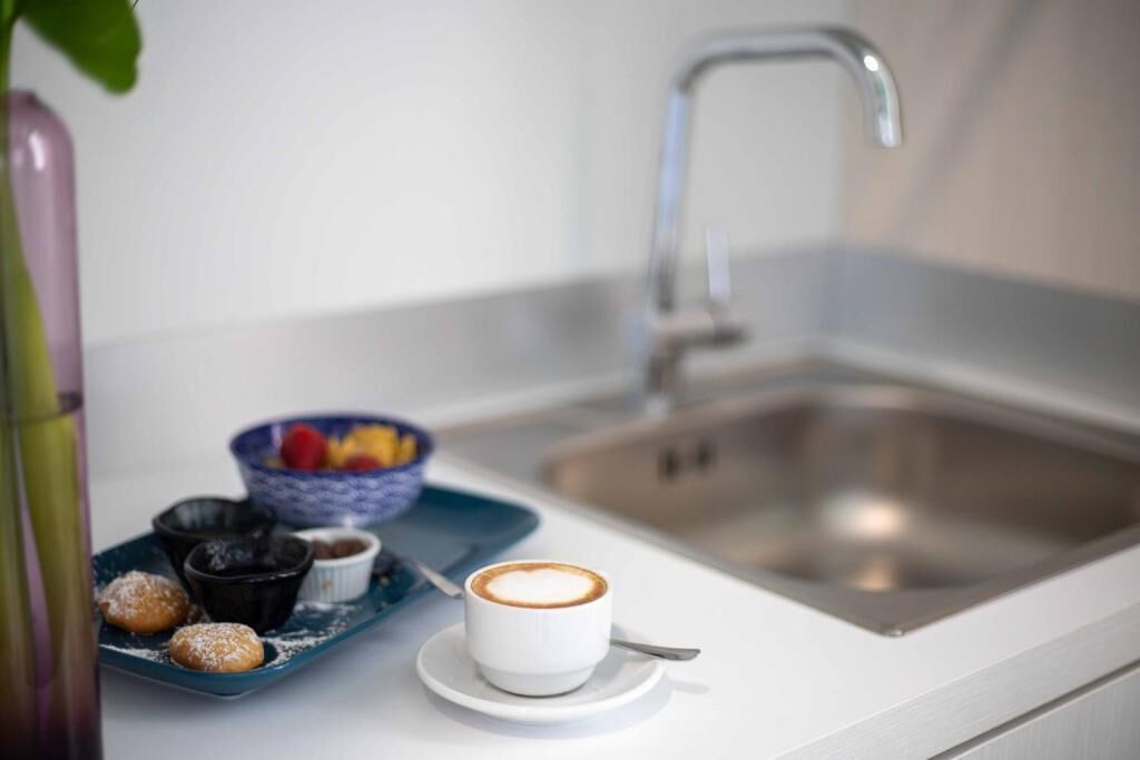 A kitchen counter with a coffee cup, a bowl of fruit, and a plate of pastries.