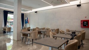 Uma sala de jantar moderna com mesas e cadeiras, um extintor de incêndio na parede e um interior limpo e bem iluminado.