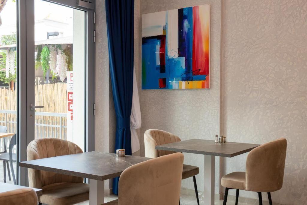 Ein modernes Interieur mit Essbereich, der zwei Tische und Stühle umfasst, einem großen abstrakten Gemälde an der Wand und Blick durch eine Glastür.