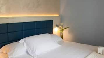 Una cama bien tendida con sábanas blancas, un cabecero azul y una lámpara de noche.