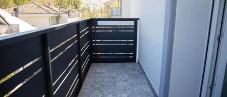 Un balcón con piso estampado, barandal negro y puerta que da a un espacio interior.