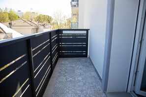 A balcony with a patterned floor, a black railing, and a door leading to an interior space.
