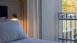 Quarto de hotel com uma cama, janela com vista para o exterior e grades de metal decorativas.