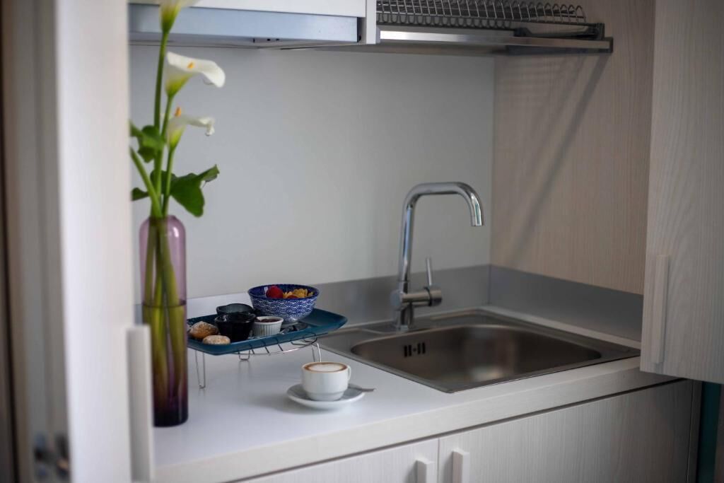 Una cocina compacta con un lavamanos de acero inoxidable, una pequeña encimera y un florero con flores blancas.