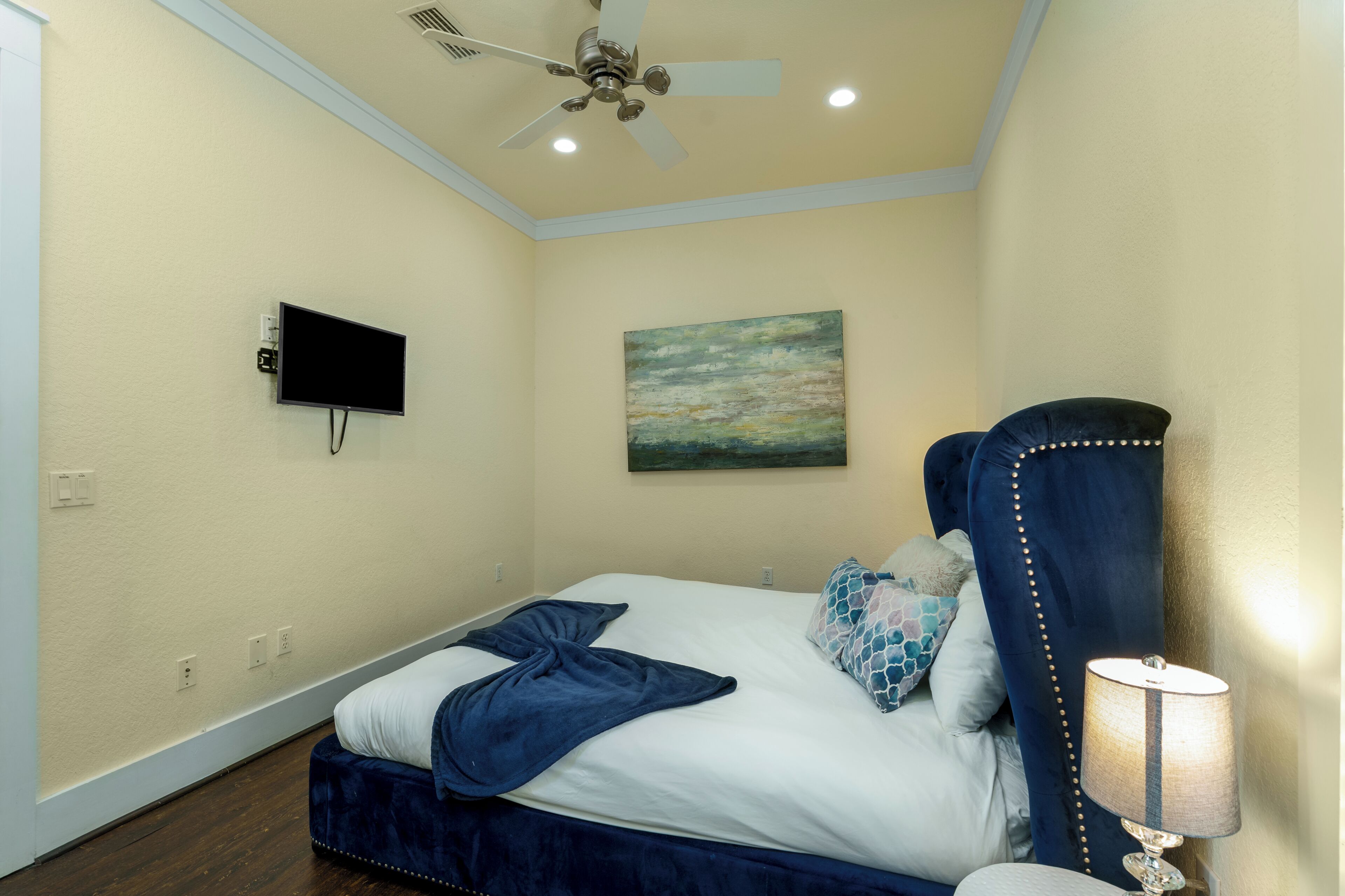 Une chambre d’hôtel avec un lit, un ventilateur de plafond, un téléviseur à écran plat et un tableau au mur.