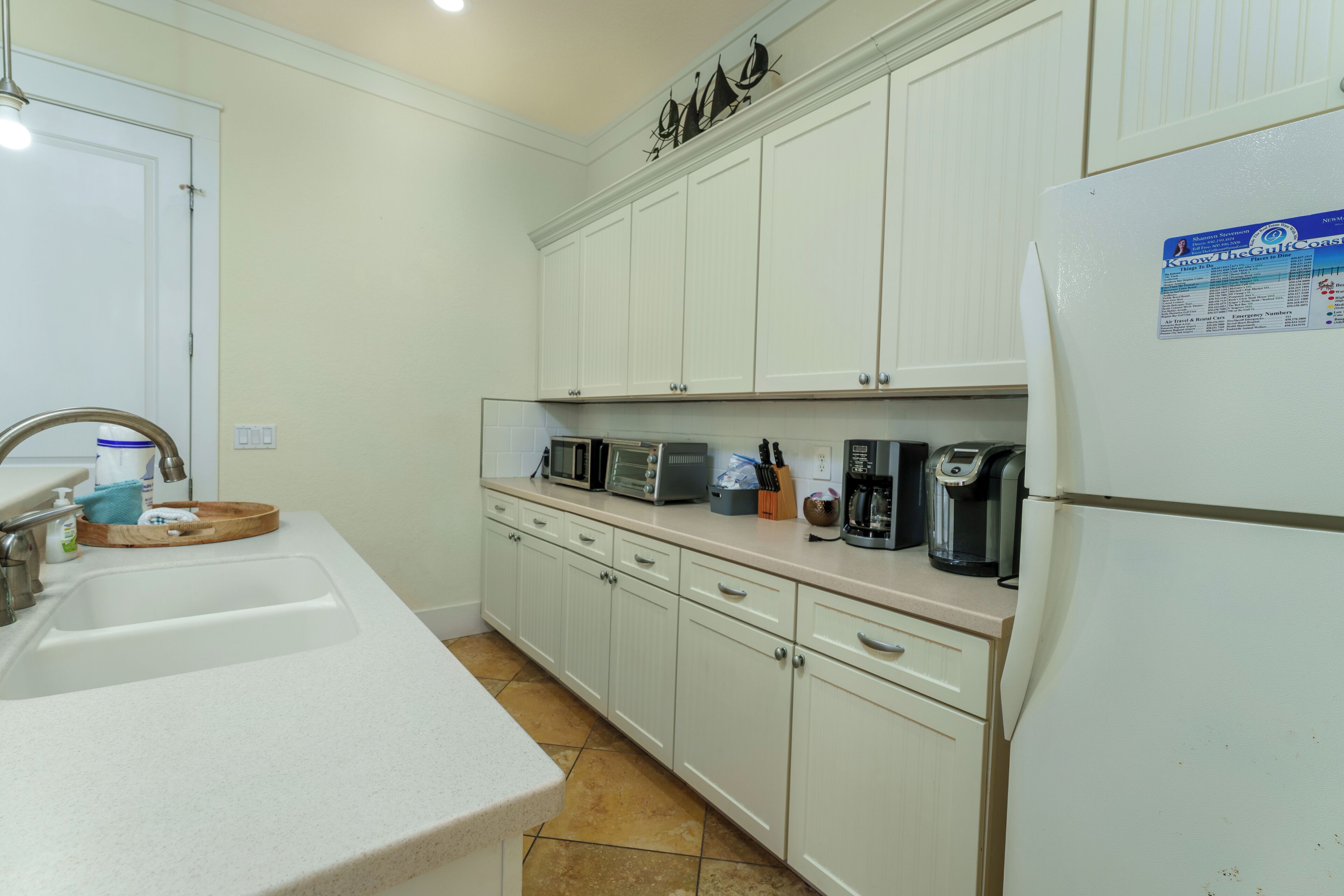 A kitchen with white cabinets, a sink, a microwave, and a coffee maker.