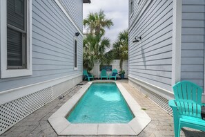 Ein rechteckiger Pool mit weißer Umrandung, umgeben von einer gepflasterten Terrasse.