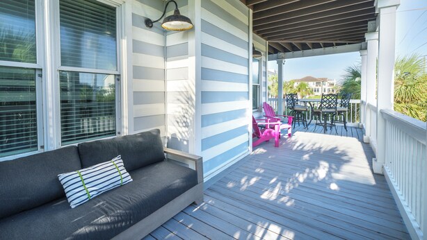A covered porch with a gray sofa, a table, and chairs. - Sandy Heels | Steps to the Beach | Pool | Pet Friendly (Destin)