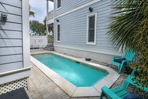 A residential swimming pool with a wooden deck, a white fence, and turquoise chairs. - Sandy Heels | 6BR Crystal Beach Home with Gulf Views, Private Pool & Steps to Beach | Sleeps 20 (Destin)