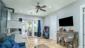 A living room with a sofa, a coffee table, a ceiling fan, a television, and a sliding glass door leading to a balcony. - Sandy Heels | Steps to the Beach | Pool | Pet Friendly (Destin)