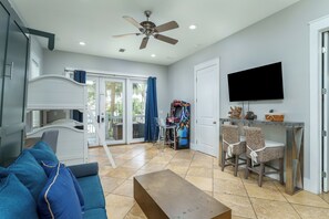 Ein Wohnzimmer mit einer Couch, einem Couchtisch, einem Deckenventilator, einem Fernseher und einer Schiebetür zum Balkon.
