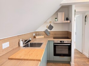 A compact kitchen with a wooden countertop, stainless steel sink, and a built-in oven. - The 37th - "The 21st Plate" Collection (Bayeux)