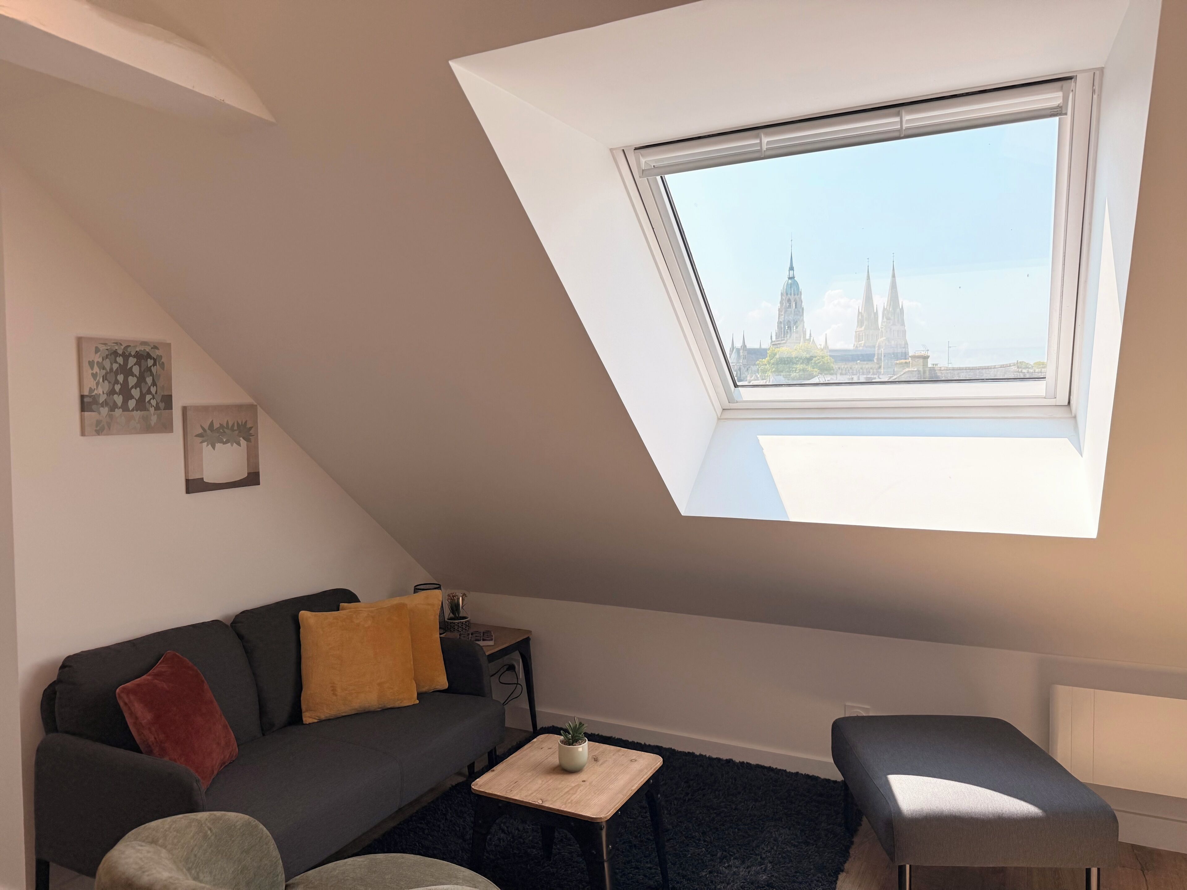 Ein modernes Wohnzimmer mit schräg versiegelter Decke, einer Couch, einem Couchtisch und Blick auf eine Stadtlandschaft durch ein Oberlicht.