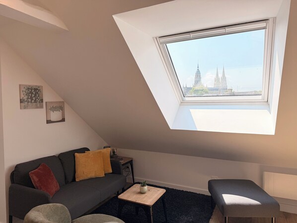 Sala de estar moderna com teto inclinado, um sofá, uma mesa de centro e vista para a cidade através de um claraboia.