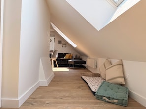 A narrow hallway with a sloped ceiling leading to a living area with a sofa, a chair, and a small table. - The 37th - "The 21st Plate" Collection (Bayeux)