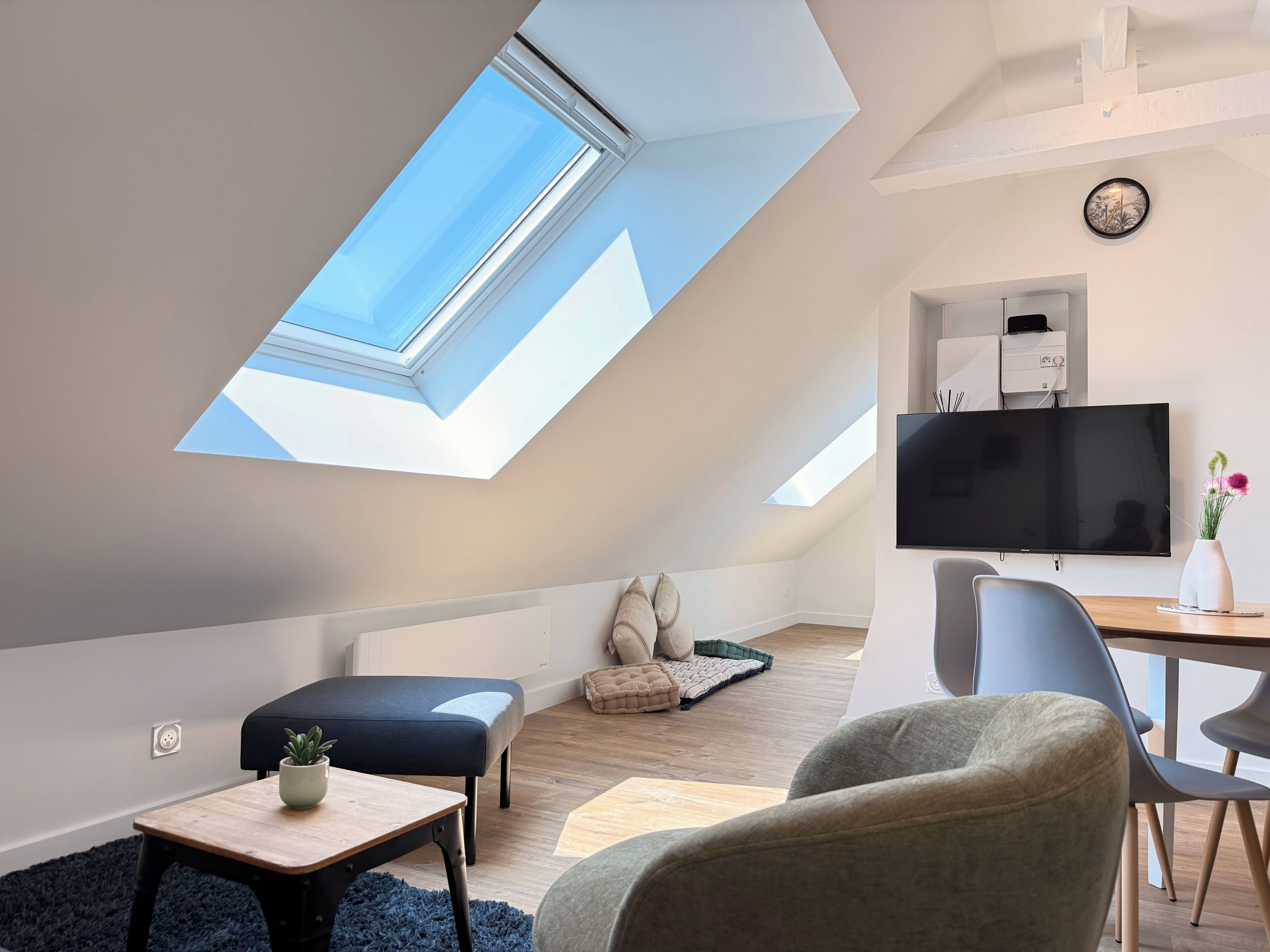 A modern loft bedroom with a skylight, a flat-screen TV, and a comfortable seating area.