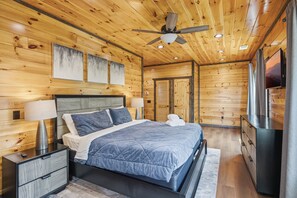A wooden-paneled bedroom with a bed, nightstands, a ceiling fan, and a TV. - Smoky Ridge Retreat | 2 Cabins, Views & Games (Sevierville)