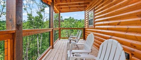 A wooden cabin with a porch, white Adirondack chairs, and a view of trees.