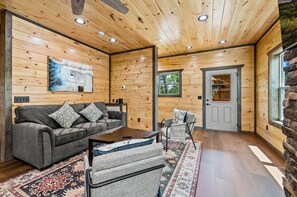 A log cabin interior with a sofa, armchairs, a coffee table, and a rug. - Smoky Ridge Retreat | 2 Cabins, Views & Games (Sevierville)