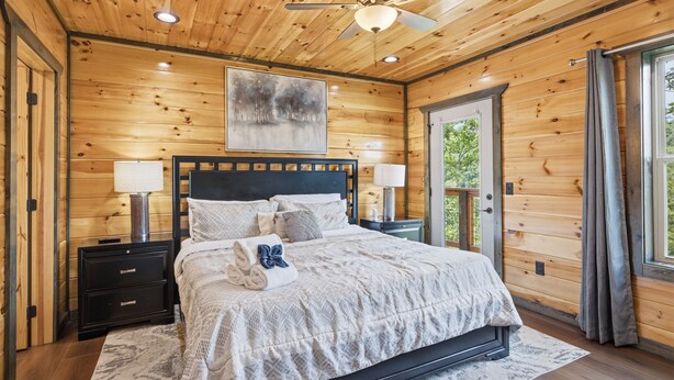 Een slaapkamer met houten lambrisering, een bed, twee nachtkastjes, een plafondventilator en een raam met gordijnen.