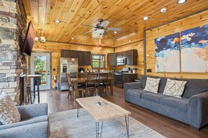 A log cabin interior with a dining area, kitchen, living room, and a large abstract painting. - Smoky Ridge Retreat | 2 Cabins, Views & Games (Sevierville)