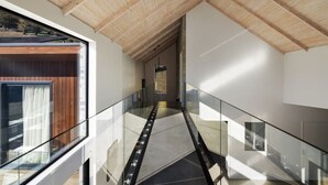 A modern interior with a glass railing, wooden ceiling, and a view through a window.