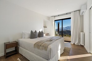 Ein Schlafzimmer mit einem großen Bett, einem Nachttisch, einem Fenster mit Bergblick und einer Schiebeglastür.