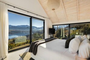 A bedroom with a large bed, a television, and a scenic view of mountains and a lake. - Noa by the Lake Queenstown by MajorDomo | Grand Lakefront Retreat for 14 with Spa Pool, Pilates Studio & Private Gym (Lake Hayes Estate)