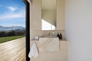 Ein modernes Badezimmer mit Marmorwaschbecken, einem großen Spiegel und Blick auf eine Berglandschaft.