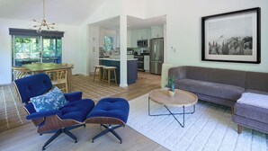 Ein großzügiger Wohnbereich mit Esstisch, blau gepolsterten Stühlen, einem grauen Sofa und einer Küche im Hintergrund.