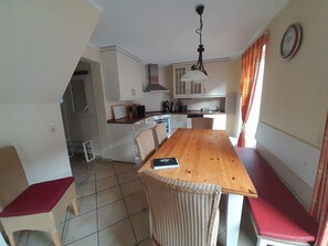 A compact kitchen with white cabinets, a wooden dining table, and a red cushion on a chair. - Gemutliches Ferienhaus mit Terrasse Nahe dem Muritzsee in Rechlin (Rechlin)