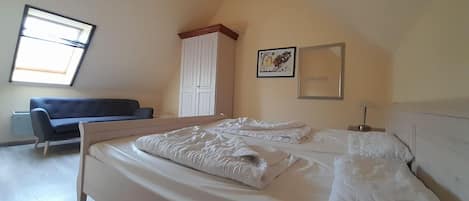 A bedroom with a bed, a sofa, a wardrobe, and a window.
