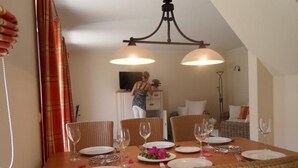 A dining area with a wooden table set for four, surrounded by wicker chairs, and a television in the background. - Gemutliches Ferienhaus mit Terrasse Nahe dem Muritzsee in Rechlin (Rechlin)