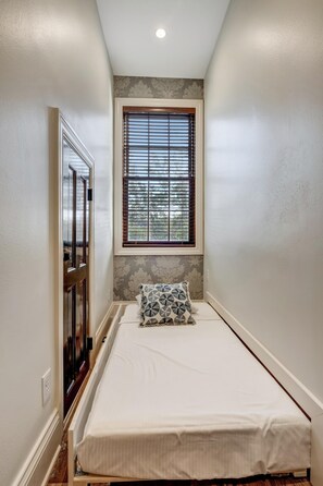 A narrow room with a bed, a window with blinds, a door, and a small wall-mounted shelf. - 2 Bedroom condo at Fisherman’s Wharf inside Sandestin Golf and Beach Resort (Miramar Beach)