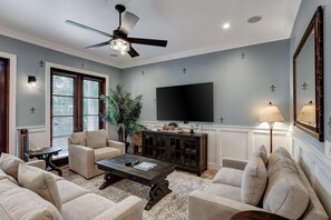 A living room with a ceiling fan, a flat-screen TV, a coffee table, and beige sofas. - 2 Bedroom condo at Fisherman’s Wharf inside Sandestin Golf and Beach Resort (Miramar Beach)