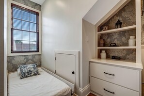 Een slaapkamer met een bed, een raam met zonwering, een dressoir met laden en een plank met decoratieve objecten.