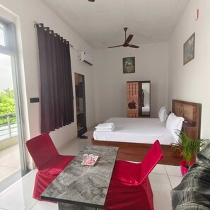 Quarto de hotel com cama, mesa e cadeiras, ventilador de teto, janela com cortinas e varanda.
